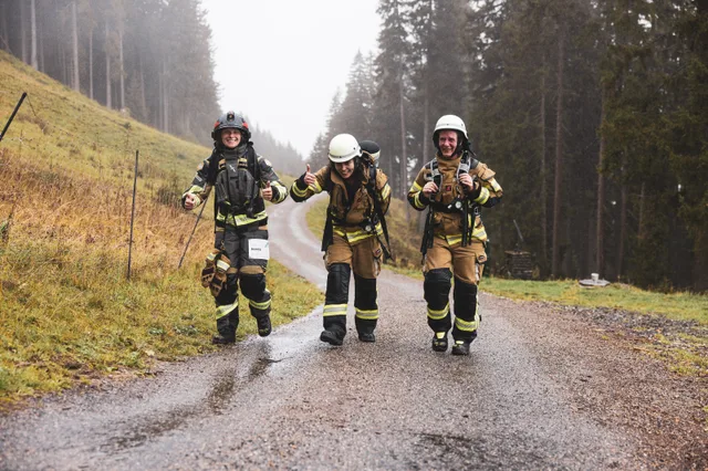 Drei Teilnehmer in Einsatzkleidung gehen auf der nassen Bergstraße bergauf.
