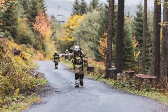 Teilnehmer in beiger Einsatzkleidung auf der nassen Bergstraße im Herbstwald.
