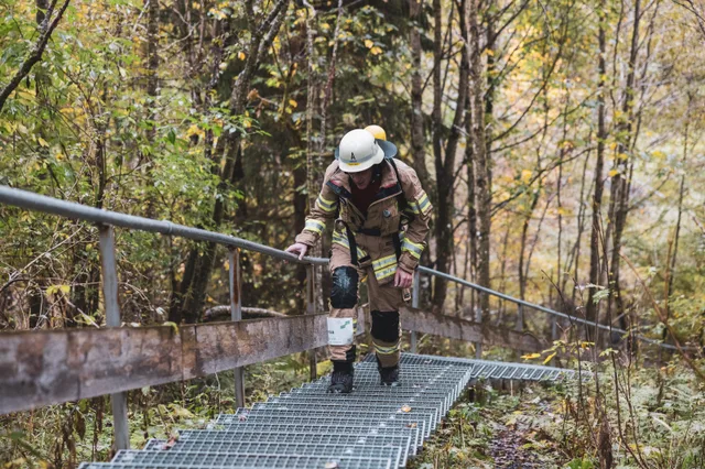 Teilnehmer in beiger Einsatzkleidung auf einer Metalltreppe zwischen Bäumen.