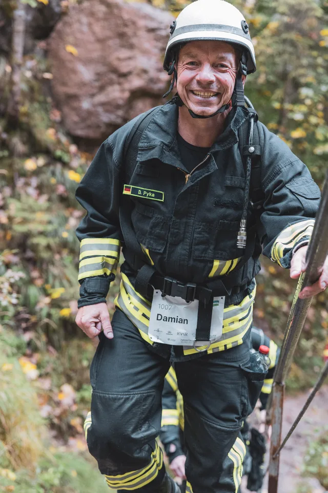 Lächelnder Teilnehmer in dunkler Einsatzkleidung auf den Waldstufen.