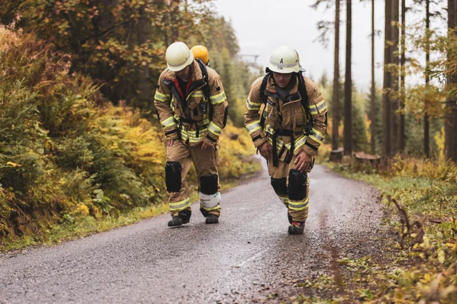 Zwei Teilnehmer in beiger Einsatzkleidung gehen nebeneinander die nasse Bergstraße hinauf.