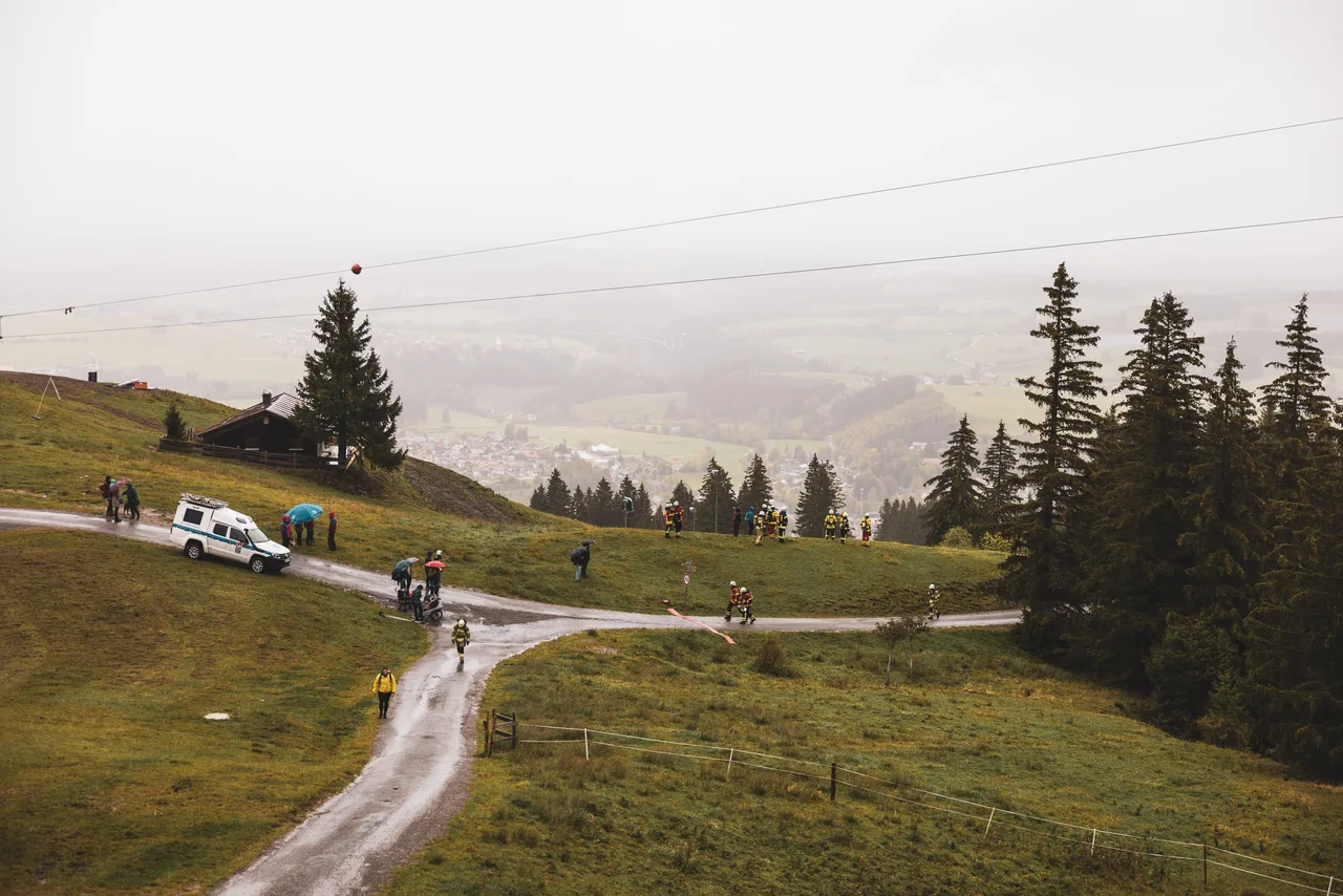 Teilnehmer und Zuschauer mit Regenschirmen an nassen Bergwegen oberhalb von Nesselwang.