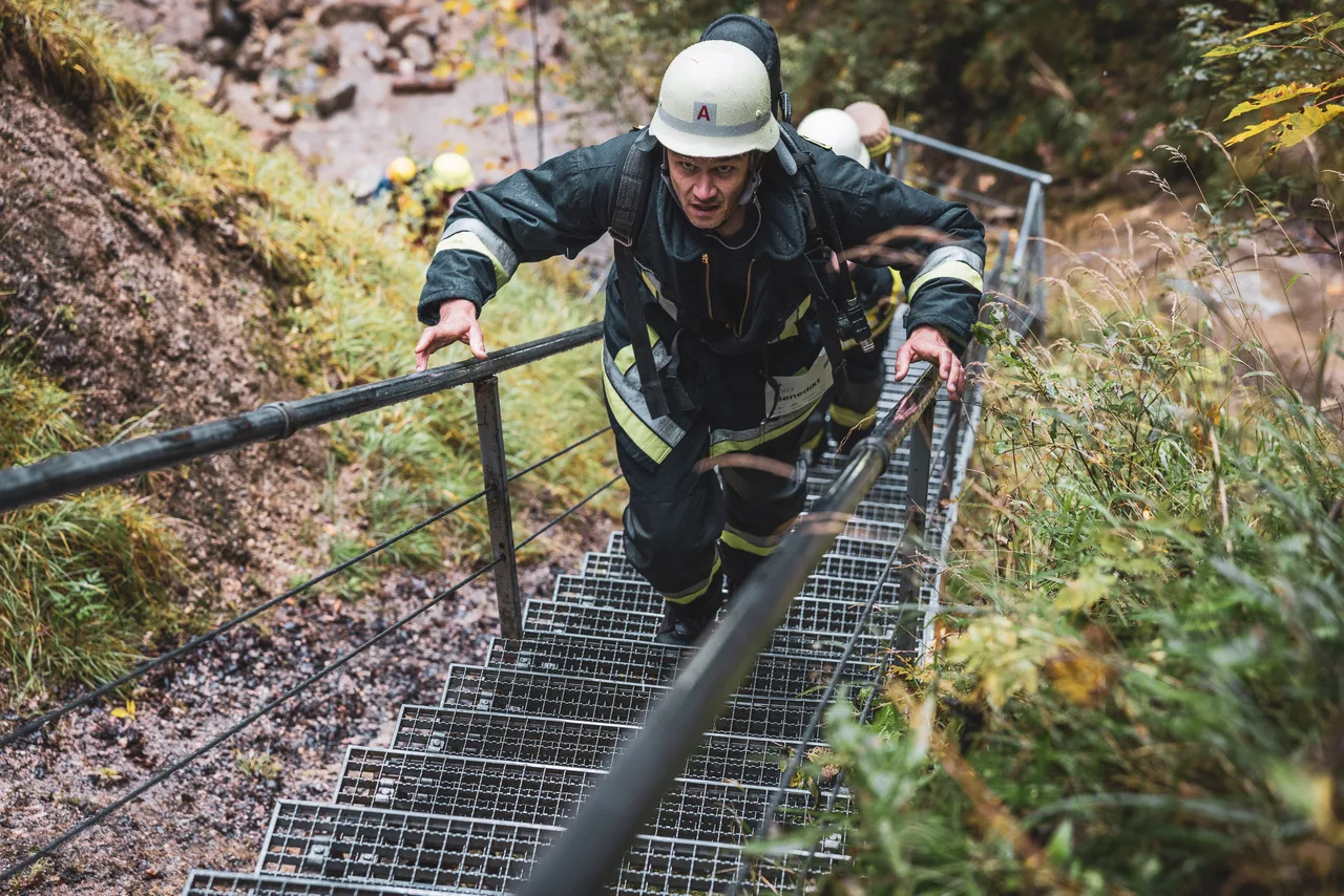 Teilnehmer in schwarzer Einsatzkleidung und weißem Helm steigt die Waldtreppe hinauf.