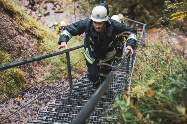 Teilnehmer in schwarzer Einsatzkleidung und weißem Helm steigt die Waldtreppe hinauf.