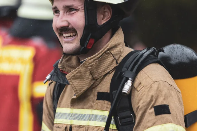 Lachender Teilnehmer in beiger Einsatzkleidung mit Helm.