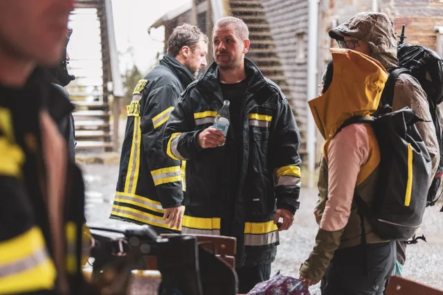 Teilnehmer mit Getränken vor der Holzwand des Sportheims.