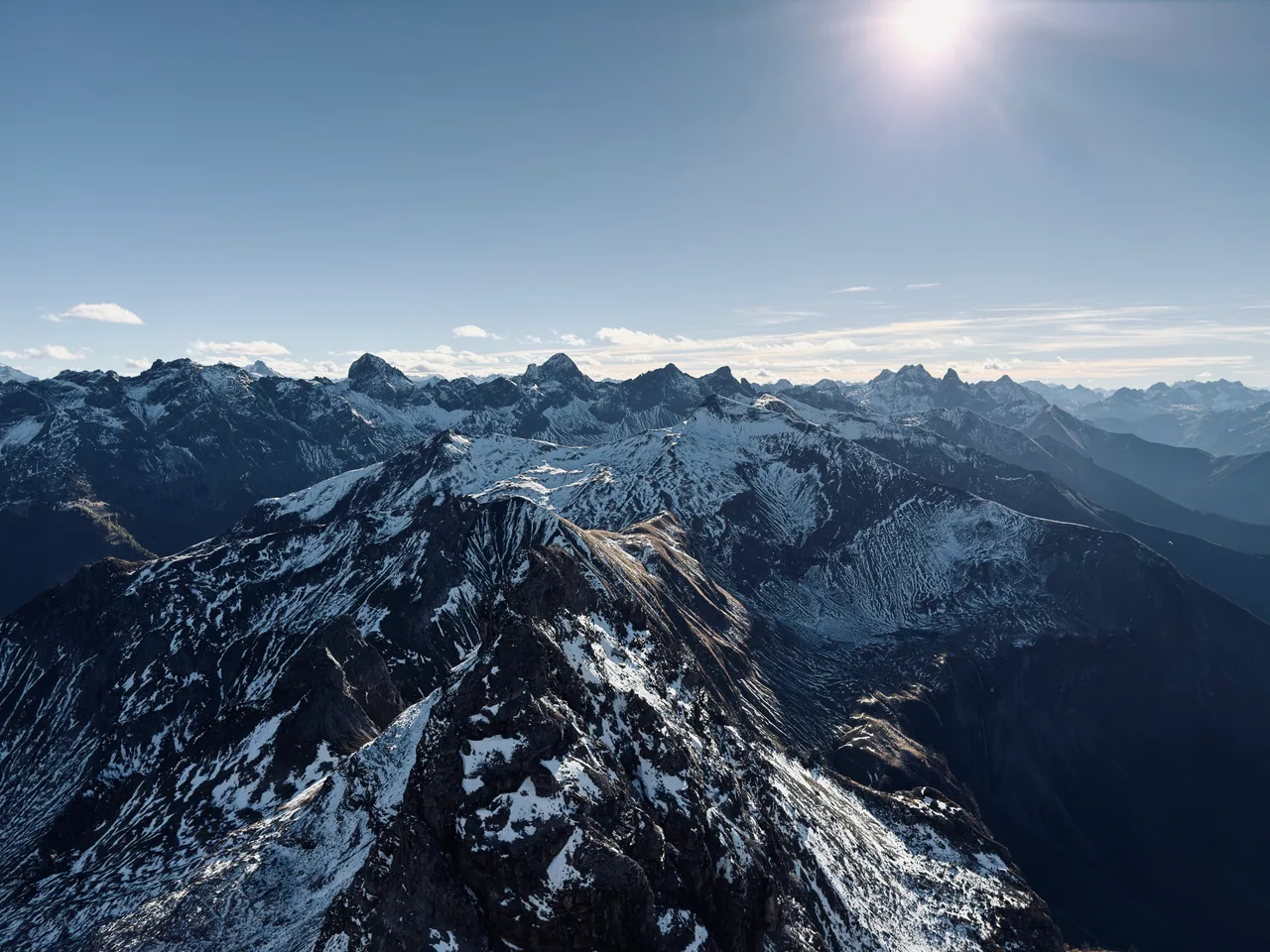 Verschneite Berggrate und gestaffelte Alpengipfel unter der Herbstsonne, aus der Luft gesehen