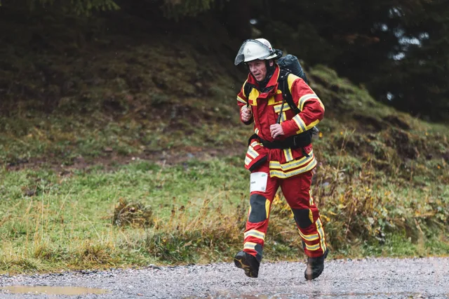 Teilnehmer in roter Einsatzkleidung läuft über den nassen Schotter ins Ziel.