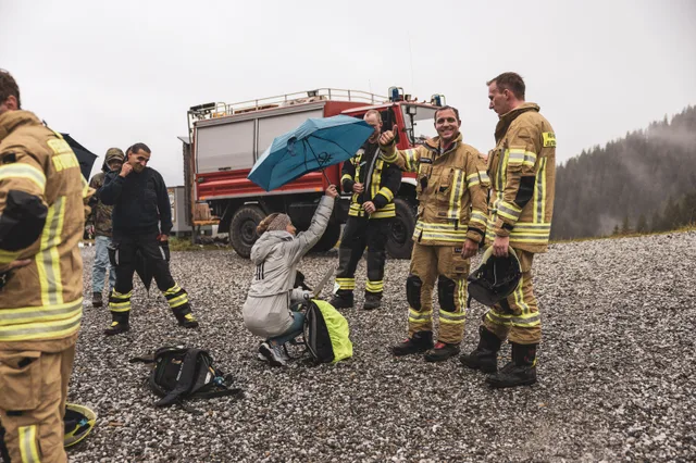 Teilnehmer und Zuschauer mit Regenschirmen vor einem Feuerwehrfahrzeug.