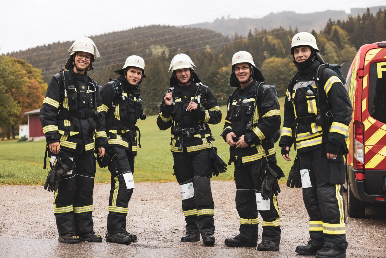 Fünf Feuerwehrleute in Schutzkleidung und mit Atemschutzgeräten stehen neben einem Einsatzfahrzeug.