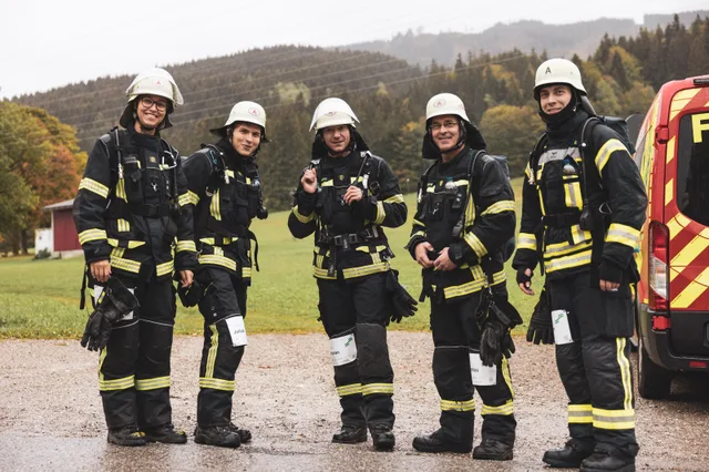 Fünf Feuerwehrleute in Schutzkleidung und mit Atemschutzgeräten stehen neben einem Einsatzfahrzeug.
