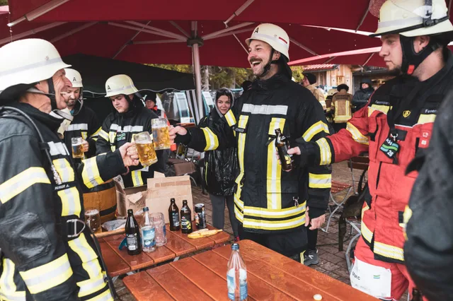 Lachende Teilnehmer stehen mit Getränken unter einem Schirm.