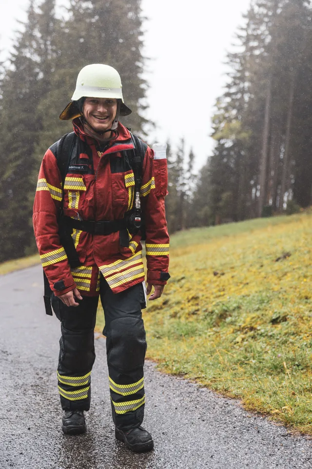 Teilnehmer in roter Einsatzkleidung und weißem Helm auf der nassen Bergstraße.