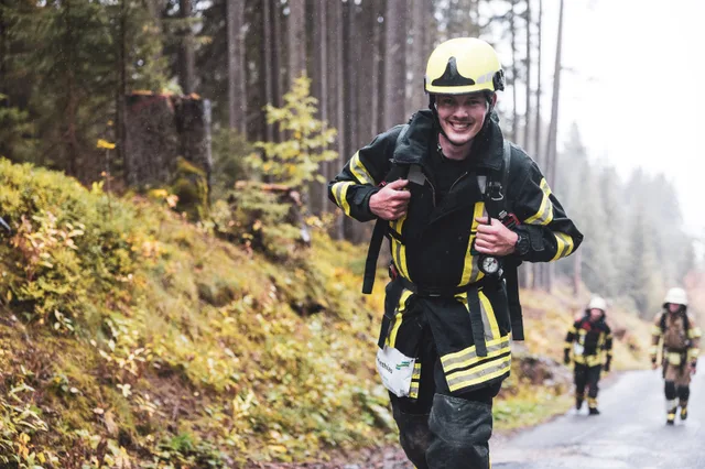 Lachender Teilnehmer mit gelbem Helm hält beim Aufstieg die Tragegurte.