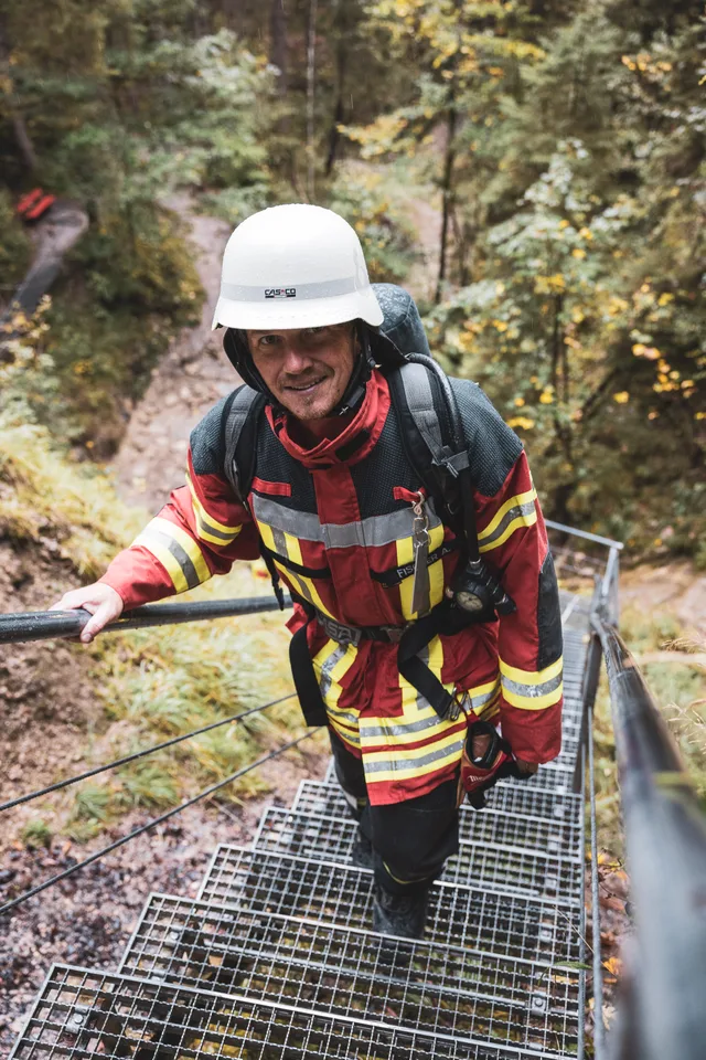 Teilnehmer in roter Einsatzkleidung und weißem Helm auf einer Metalltreppe.