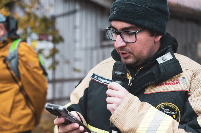 Teilnehmer mit Strickmütze spricht ins Mikrofon und hält ein Mobiltelefon.