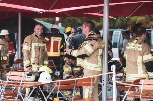 Teilnehmer in beiger Einsatzkleidung ruhen unter einem roten Schirm aus.