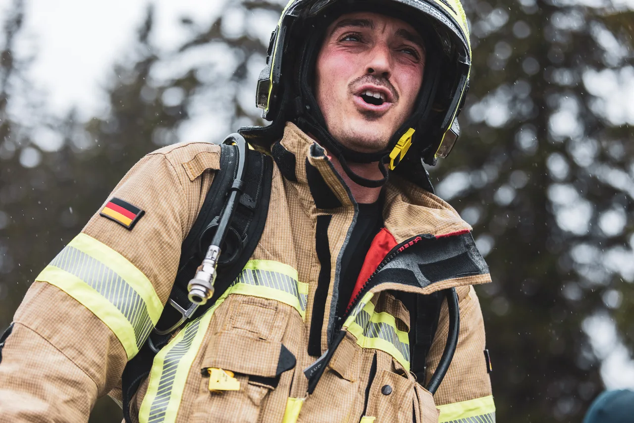 Nahaufnahme eines Feuerwehrmanns mit regennassem Helm und geöffnetem Mund beim Berglauf.